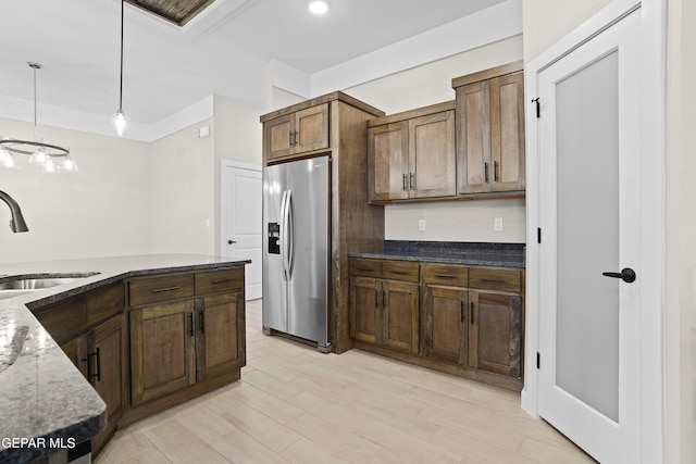 kitchen featuring stainless steel refrigerator with ice dispenser, hanging light fixtures, sink, light wood-type flooring, and dark stone countertops