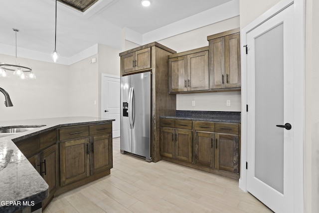 kitchen featuring decorative light fixtures, a sink, stainless steel fridge, dark stone counters, and recessed lighting