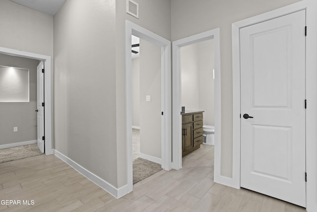 hall featuring visible vents, baseboards, and light wood-type flooring