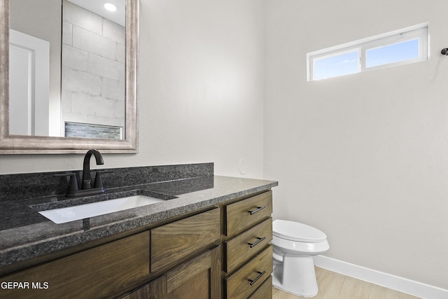 bathroom featuring vanity, baseboards, wood finished floors, and toilet