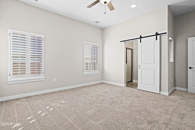 unfurnished bedroom with light colored carpet, a barn door, and ceiling fan