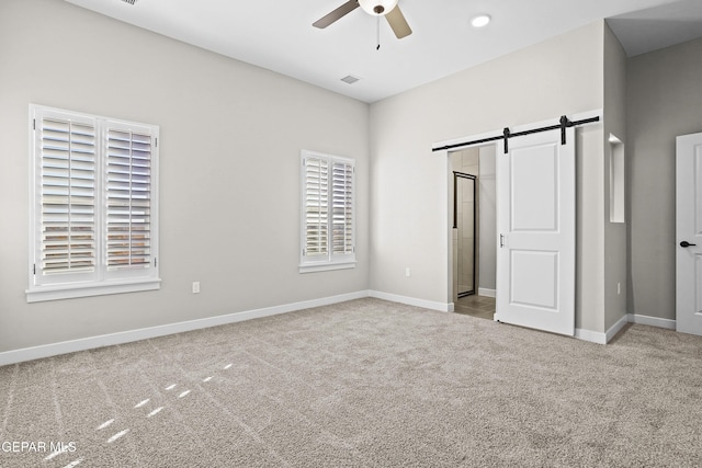 unfurnished bedroom with ceiling fan, visible vents, a barn door, baseboards, and carpet flooring