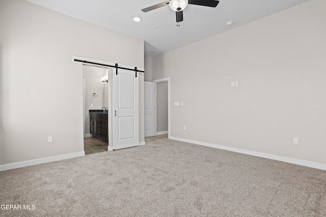 unfurnished bedroom featuring connected bathroom, a barn door, light colored carpet, and ceiling fan