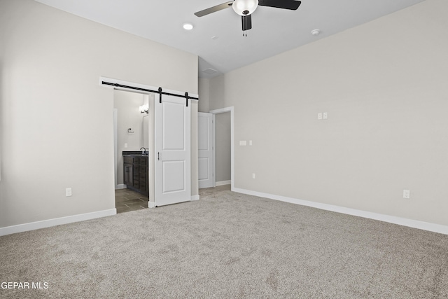 unfurnished bedroom with a ceiling fan, a barn door, baseboards, ensuite bathroom, and carpet flooring