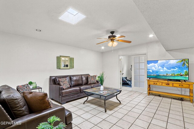 living room featuring light tile patterned flooring, a textured ceiling, a skylight, and ceiling fan