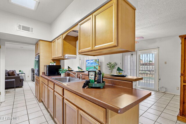 kitchen featuring light brown cabinetry, sink, a textured ceiling, and light tile patterned floors