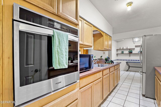 kitchen with sink, light tile patterned floors, light brown cabinets, and stainless steel appliances