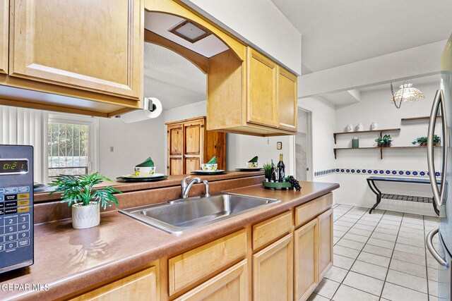 kitchen with light tile patterned flooring, sink, stainless steel refrigerator, and light brown cabinets