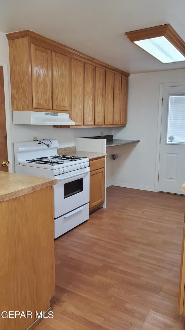 kitchen featuring under cabinet range hood, white range with gas stovetop, light countertops, and light wood-style floors