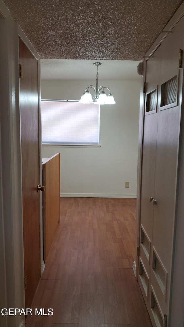 corridor featuring a textured ceiling, baseboards, wood finished floors, and an inviting chandelier