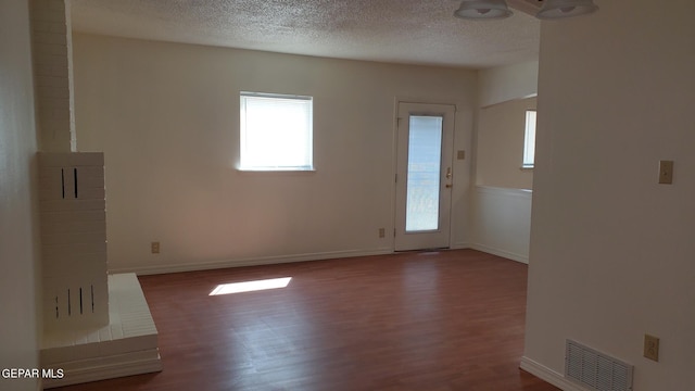 unfurnished room with dark wood-style flooring, visible vents, a textured ceiling, and baseboards