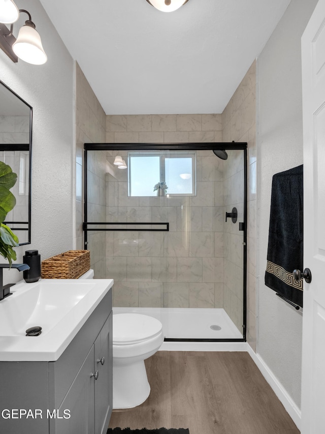 bathroom featuring wood-type flooring, vanity, a shower with shower door, and toilet