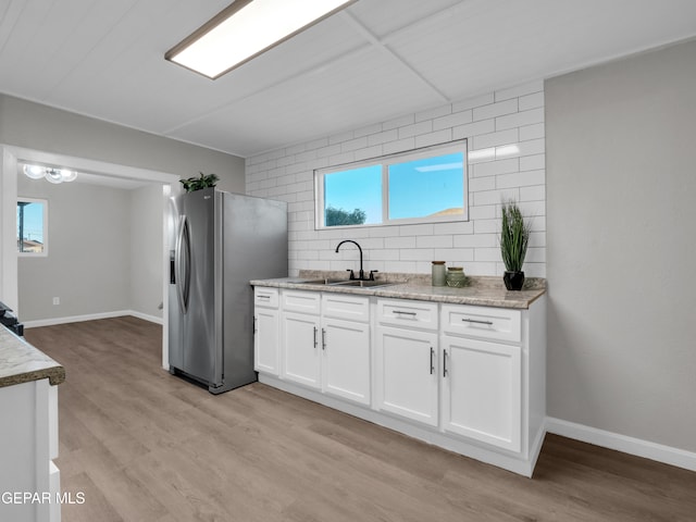 kitchen featuring white cabinets, light stone countertops, stainless steel fridge, sink, and light wood-type flooring