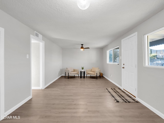 sitting room featuring light wood-type flooring, ceiling fan, and a textured ceiling