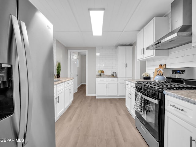 kitchen with white cabinets, wall chimney exhaust hood, decorative backsplash, light hardwood / wood-style flooring, and appliances with stainless steel finishes