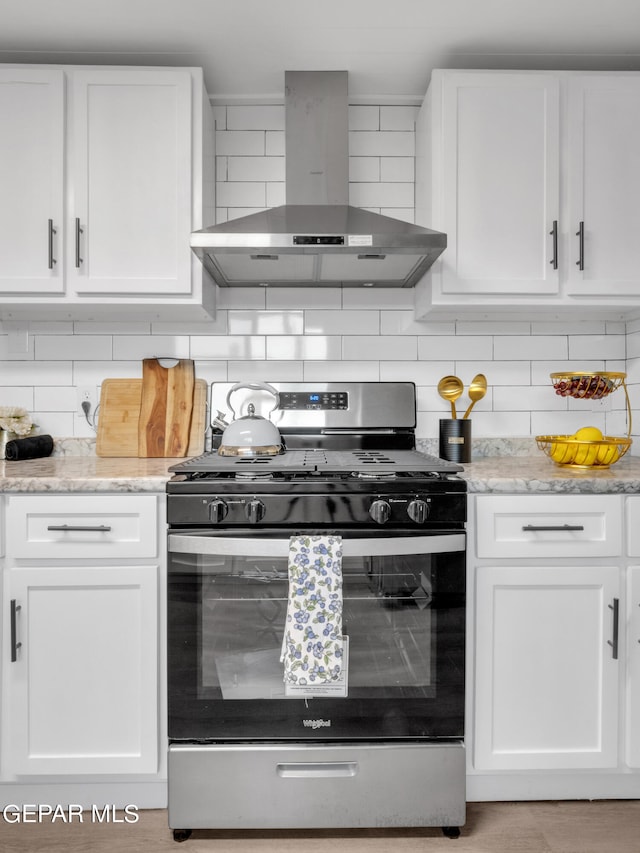 kitchen with wall chimney exhaust hood, stainless steel gas range oven, tasteful backsplash, and white cabinets