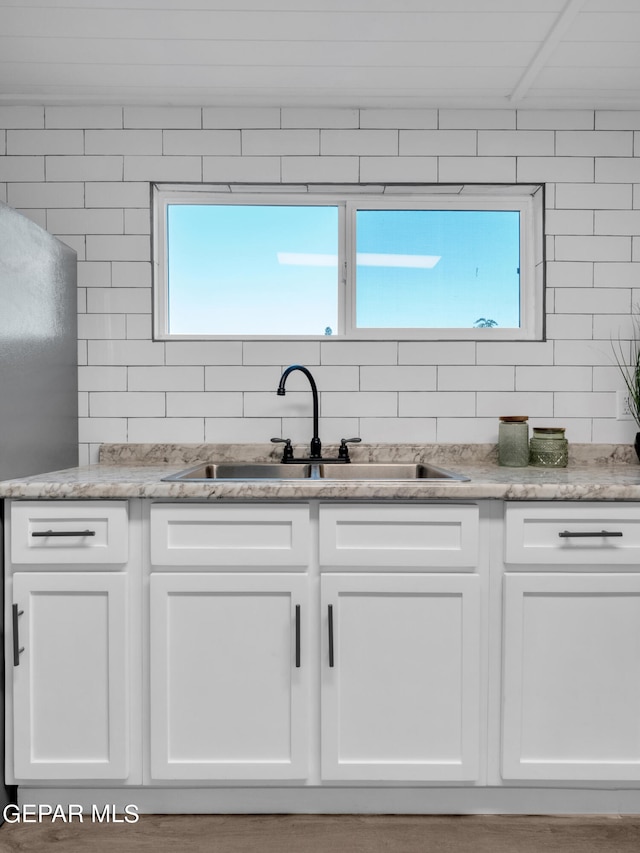 kitchen featuring a wealth of natural light, white cabinets, light stone counters, and sink