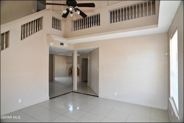 empty room with light tile patterned floors, ceiling fan, and a towering ceiling