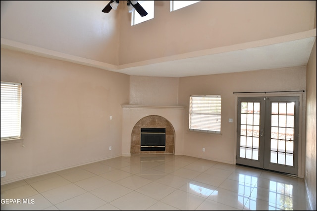 unfurnished living room with french doors, light tile patterned floors, a tiled fireplace, ceiling fan, and a towering ceiling