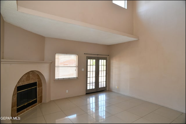 unfurnished living room with light tile patterned flooring, a tiled fireplace, and french doors