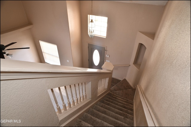 stairs featuring dark colored carpet, ceiling fan, a healthy amount of sunlight, and a towering ceiling