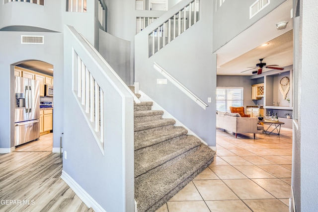 stairs featuring tile patterned flooring, ceiling fan, and a towering ceiling