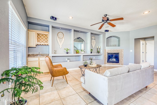 living room with a textured ceiling, ceiling fan, sink, a fireplace, and light tile patterned flooring