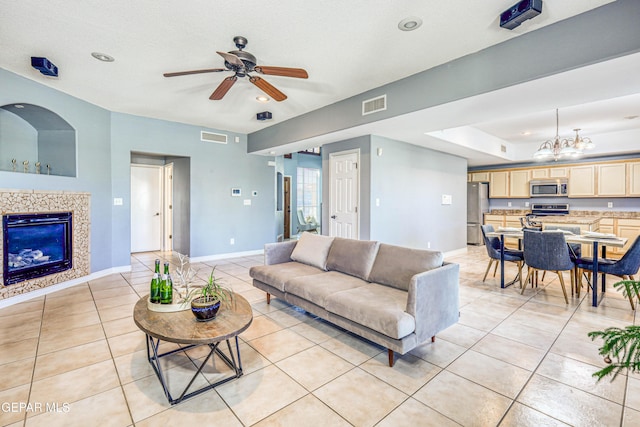 tiled living room featuring a textured ceiling, a raised ceiling, a fireplace, and ceiling fan with notable chandelier