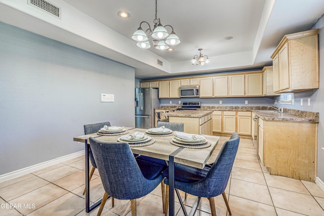 kitchen featuring a raised ceiling, light brown cabinetry, a kitchen island, stainless steel appliances, and a chandelier