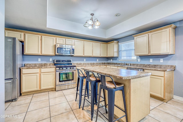 kitchen featuring a breakfast bar area, light tile patterned flooring, a tray ceiling, a kitchen island, and appliances with stainless steel finishes