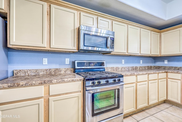 kitchen with cream cabinets, light tile patterned floors, and stainless steel appliances