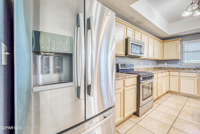 kitchen featuring a tray ceiling, sink, light tile patterned floors, and stainless steel appliances