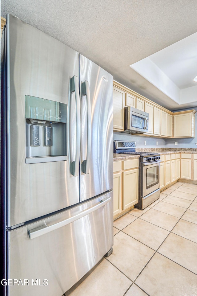 kitchen with a textured ceiling, stainless steel appliances, a tray ceiling, and light tile patterned flooring