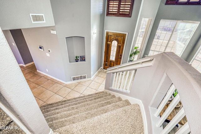 stairs with tile patterned floors and a towering ceiling