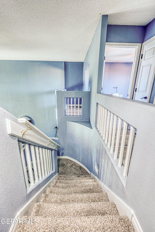 staircase featuring carpet floors and a textured ceiling