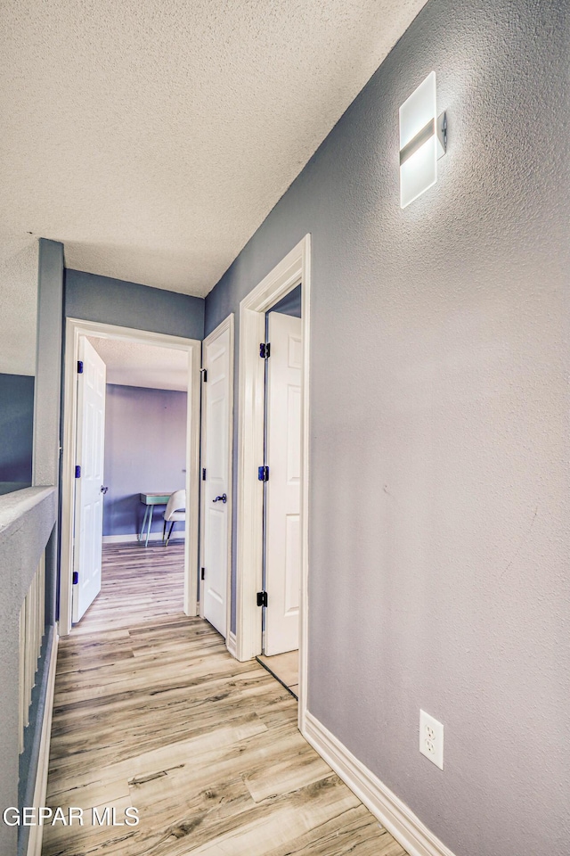 hall with a textured ceiling and light hardwood / wood-style flooring