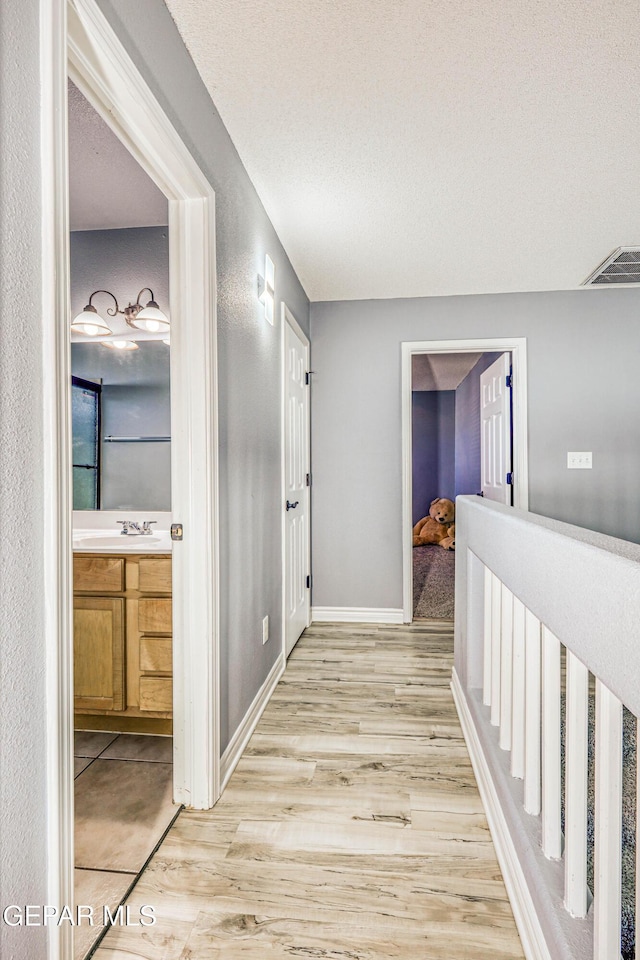 hallway featuring light hardwood / wood-style floors, sink, and a textured ceiling