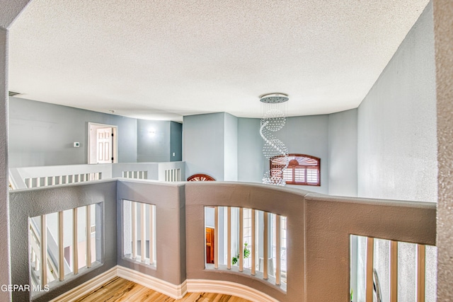 corridor with a textured ceiling, hardwood / wood-style flooring, and a notable chandelier