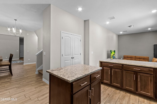 kitchen with light wood-type flooring, a kitchen island, hanging light fixtures, light stone counters, and a notable chandelier