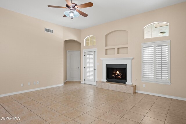 unfurnished living room featuring a towering ceiling, ceiling fan, a healthy amount of sunlight, and light tile patterned floors