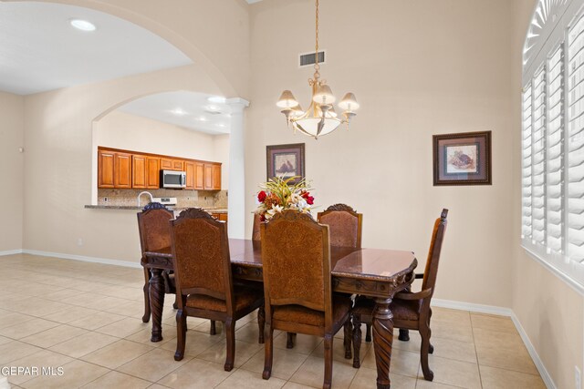 dining room with light tile patterned flooring, decorative columns, a chandelier, a high ceiling, and sink