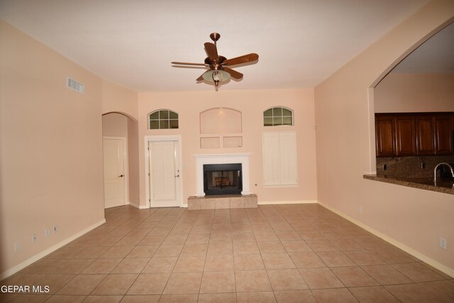 unfurnished living room featuring a tile fireplace, sink, light tile patterned floors, and ceiling fan