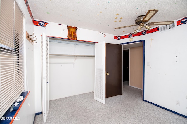 unfurnished bedroom featuring a closet, a textured ceiling, light carpet, and ceiling fan