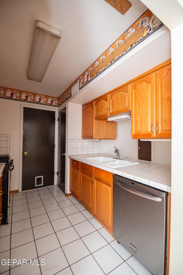 kitchen featuring stainless steel appliances, sink, light tile patterned floors, tile counters, and decorative backsplash