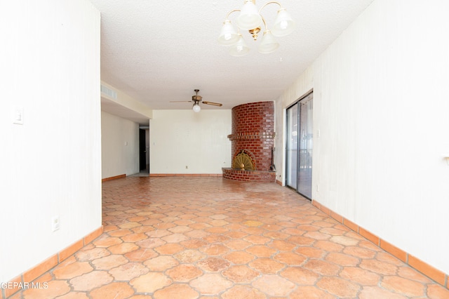 empty room with a brick fireplace, ceiling fan with notable chandelier, and a textured ceiling