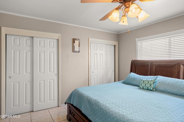 bedroom with light tile patterned floors, ceiling fan, ornamental molding, and two closets