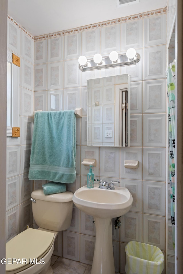 bathroom with toilet, a sink, visible vents, and tile walls