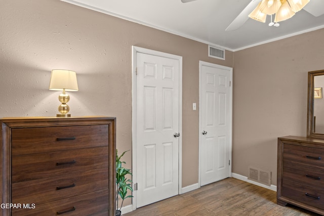 bedroom with baseboards, wood finished floors, visible vents, and crown molding