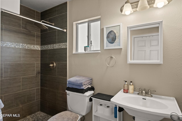 bathroom featuring tiled shower, sink, and toilet