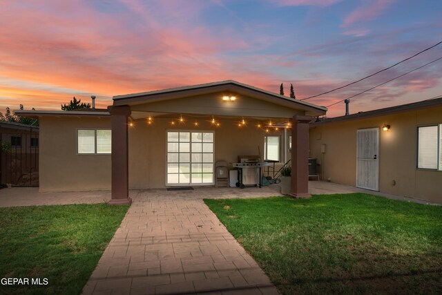 back house at dusk featuring a lawn and a patio area